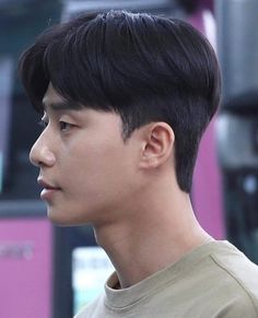 a young man with black hair standing in front of a pink bus and looking off into the distance