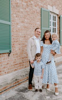 a family poses for a photo in front of a brick building with green shutters