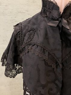 1800 vintage, half cape in black silk brocade with black beads designs trimmed in black lace. The lace around the bottom hem is wider and weightier than the lace at the high collar and around the beadwork at the shoulders. The cape is lined in silk. There is a black silk ribbon tie at the front. 2" stand up  collar, 16" from shoulder to shoulder in the back, 15" long, 3" lace trim at hem. Dry clean only Black Beads Designs, Modern Victorian Fashion, Half Cape, Costume Capes, Lace Cape, Bunny Dress, Beads Designs, Modern Victorian, Stand Up Collar