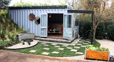 a small blue container house sitting in the middle of a yard next to a tree