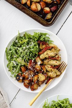 a white plate topped with chicken and salad next to a baking pan filled with potatoes