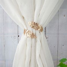 a white curtain with gold leaves on it and a green plant in the corner next to it