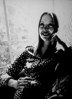 a black and white photo of a woman sitting on a couch smiling at the camera