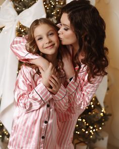 a mother and daughter hugging each other in front of a christmas tree with lights on it