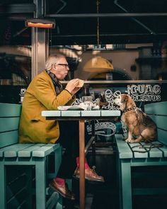 an old man sitting at a table with his dog in front of him eating food