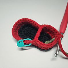 a crocheted red and black object with scissors next to it on a white surface