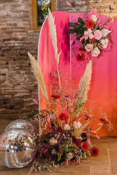 an arrangement of flowers and foliage in front of a mirror ball on the floor next to it