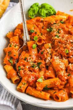 a white bowl filled with pasta and sauce on top of a table next to bread