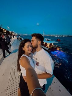 a man and woman standing next to each other on a pier near the water at night