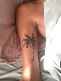 a person laying in bed with a tattoo on their arm that has a palm tree on it