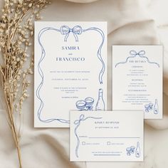 the wedding stationery is laid out on top of white fabric and features blue ink