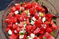 a watermelon salad with feta cheese and herbs in a glass bowl on a wooden table