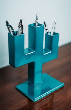 a cross shaped pen holder with three pens in it