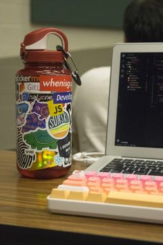 a laptop computer sitting on top of a wooden desk next to a jar filled with stickers