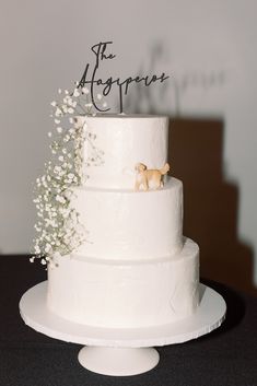 a three tiered white wedding cake with dog figurines on top and baby's breath flowers