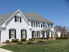 a large white house with black shutters and green grass in front of the house