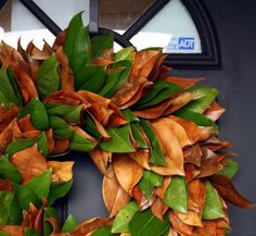 a wreath is hanging on the front door with green and brown leaves around it's edges