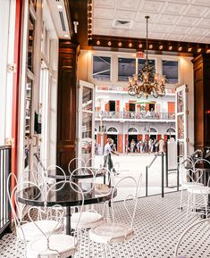 the inside of a restaurant with white chairs and black tables, chandeliers and windows