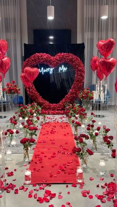 a red carpet with rose petals and candles on it in front of a heart - shaped backdrop