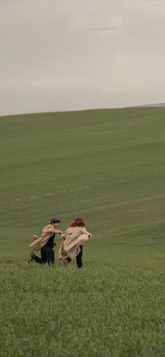 two people running in the grass with a kite