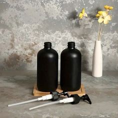 two black bottles are next to a white vase with yellow flowers in it on a wooden stand