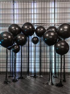 several black balloons are standing in front of a wall with metal rods and poles on the floor