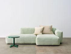 a green couch sitting on top of a cement floor next to a small round table