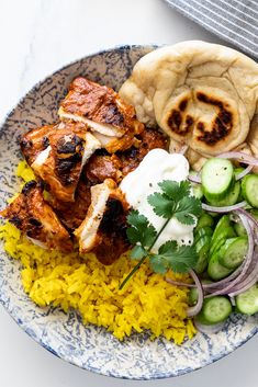 a blue and white plate topped with rice, meat and veggies next to pita bread