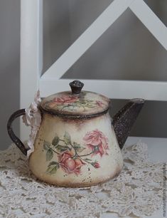 an old teapot with flowers painted on it sitting on a lace doily next to a white chair