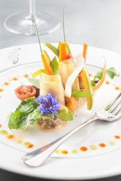 a white plate topped with different types of food next to a fork and glass of wine