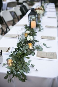 a long table with candles and greenery on it is set up for an event