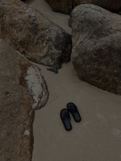 pair of black slippers on sandy beach next to large rocks