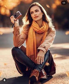 a woman sitting on the ground taking a selfie with her camera and wearing an orange scarf