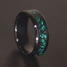 a ring with green leaves inlaying the center on a black surface, sitting on top of a wooden table