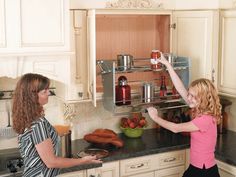 two women standing in a kitchen with food on the counter and one woman reaching for something