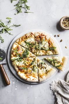 a pizza sitting on top of a white plate next to a knife and some herbs