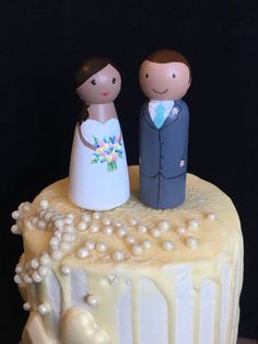 a wedding cake with two figurines standing on it's top and pearls around the edges