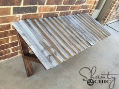 a wooden bench sitting in front of a brick wall next to a door with the words slatted chic on it