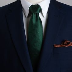 a man in a suit with a green tie and pocket square on his lapel