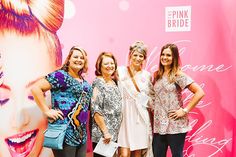 three women standing next to each other in front of a pink wall with photos on it