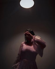 a woman in a pink dress is holding her hands up to the light above her head