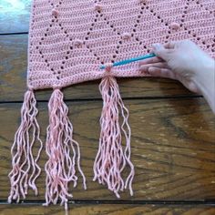 someone is crocheting a pink blanket with tassels