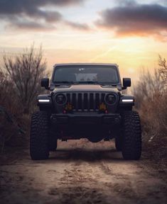 a jeep driving down a dirt road in front of the sun with trees and bushes