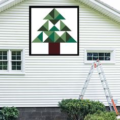 a man is painting a tree on the side of a white house with green triangles