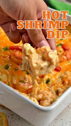 a hand holding a tortilla chip over a casserole dish with shrimp dip