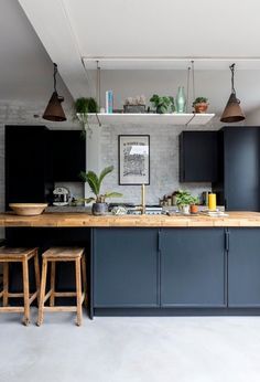 a kitchen with dark blue cabinets and wooden counter tops, hanging lights above the island