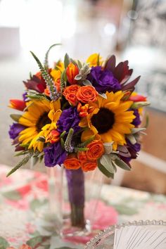 a bouquet of flowers sitting on top of a table next to a vase filled with orange and purple flowers