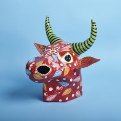 a red and white cow head with green horns on a blue background is featured in this image