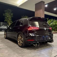 the rear end of a black car parked in front of a tall building at night