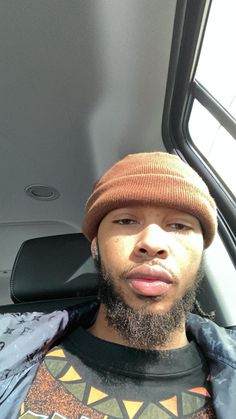 a man with a beard wearing a beanie and looking at the camera while sitting in a vehicle